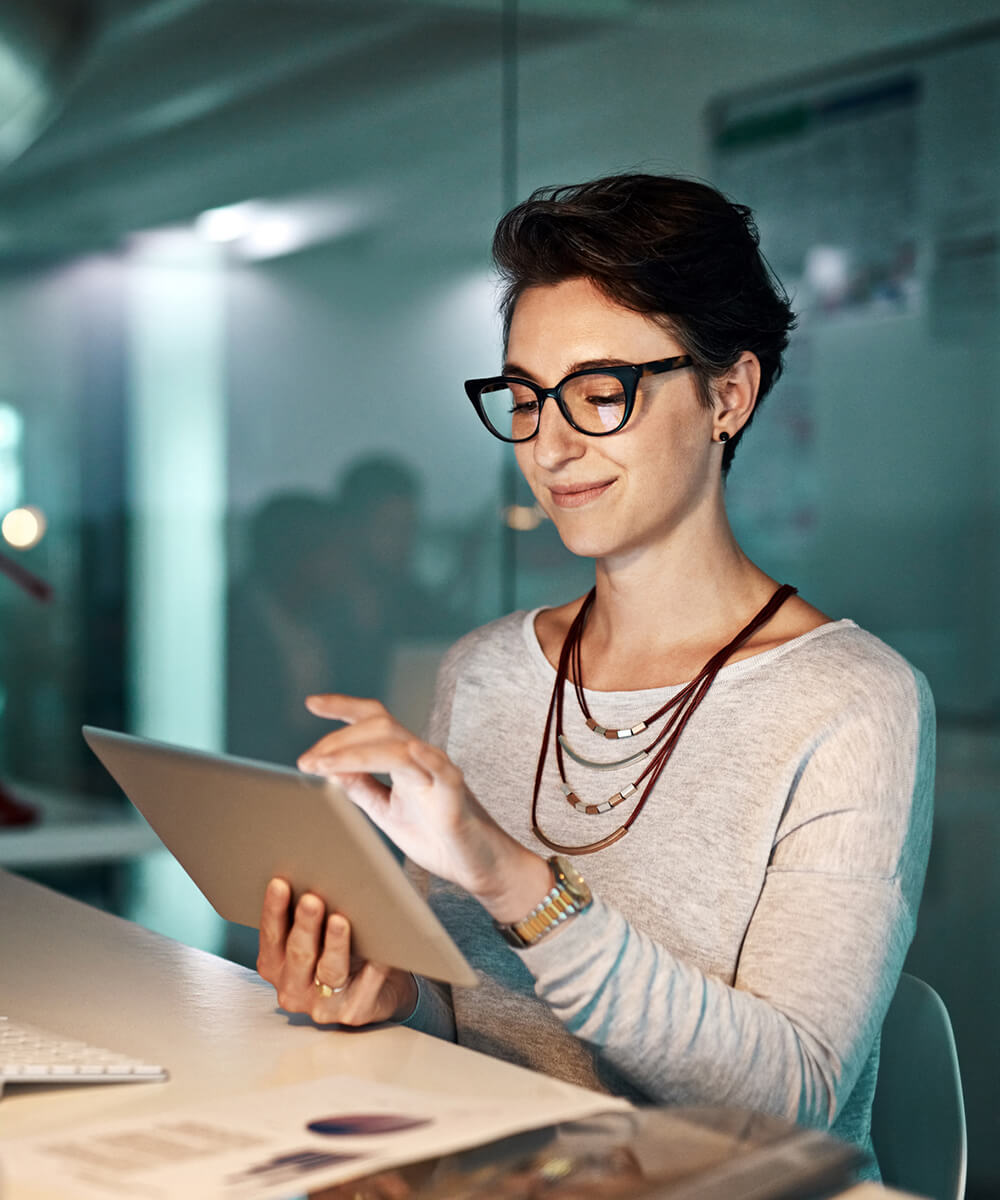 a female employee smiling while using a tablet on one hand and another hand touching the screen while sitting down in front of a table