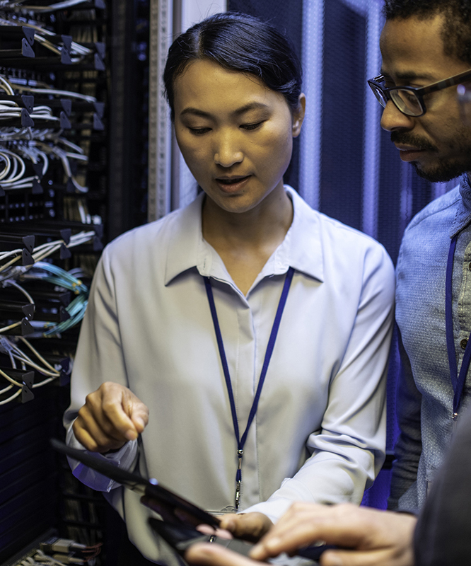 a group of network engineers discussing in front of a server rack in the server room while looking at a tablet