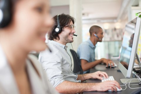 a team of workers wearing headphones with the middle man in focus smiling while watching the monitor