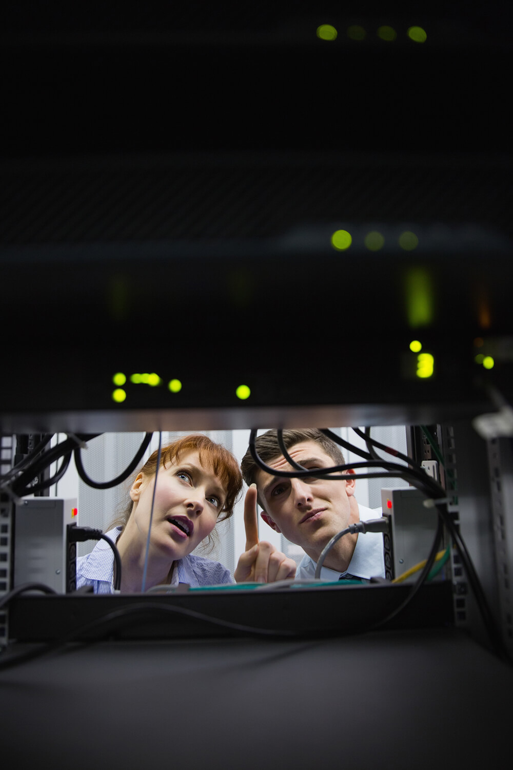 a woman pointing upwards and a man besides her looking up to where she is pointing in a server room