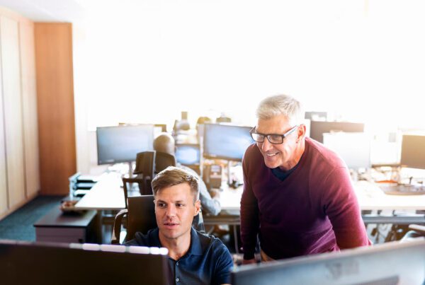 a man in blue collared t-shirt and a man in a maroon sweatshirt looking at a monitor