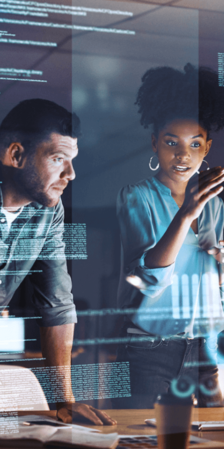 Man and woman discussing backend code while standing in front of a desk with computers