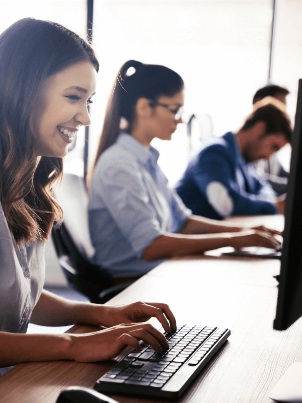 Young men and women sharing a desk while working on their computers and typing on their keywords